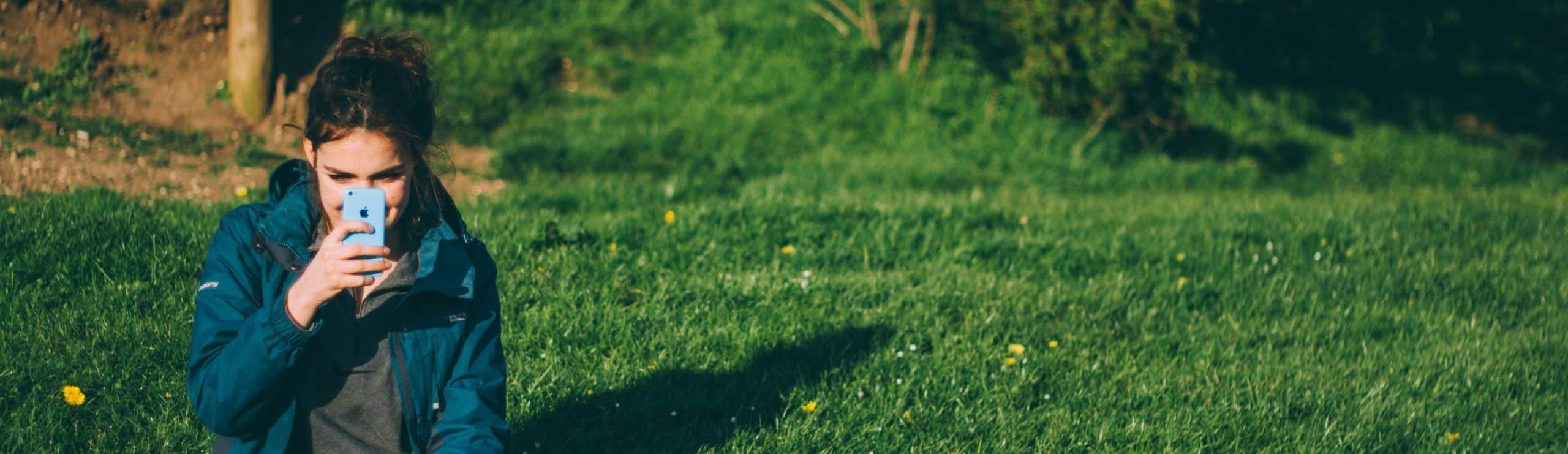 Woman taking a picture of something with her cellphone outside.