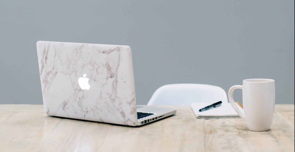 MacBook laptop on a table with a notepad and cup of coffee.