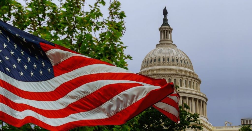 United States Capitol Building with American flag waving in front of it.