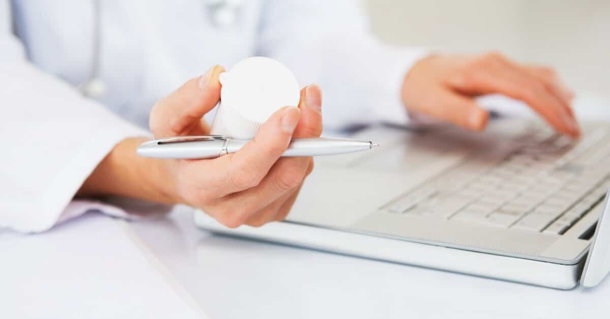 Medical professional holding medicine bottle and pen.