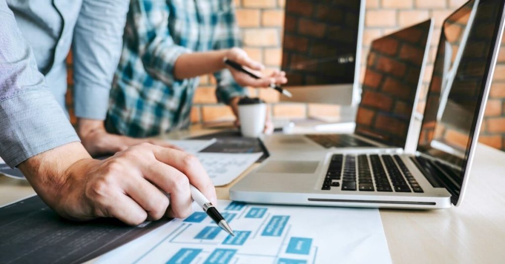 Two men collaborating on work on laptops.