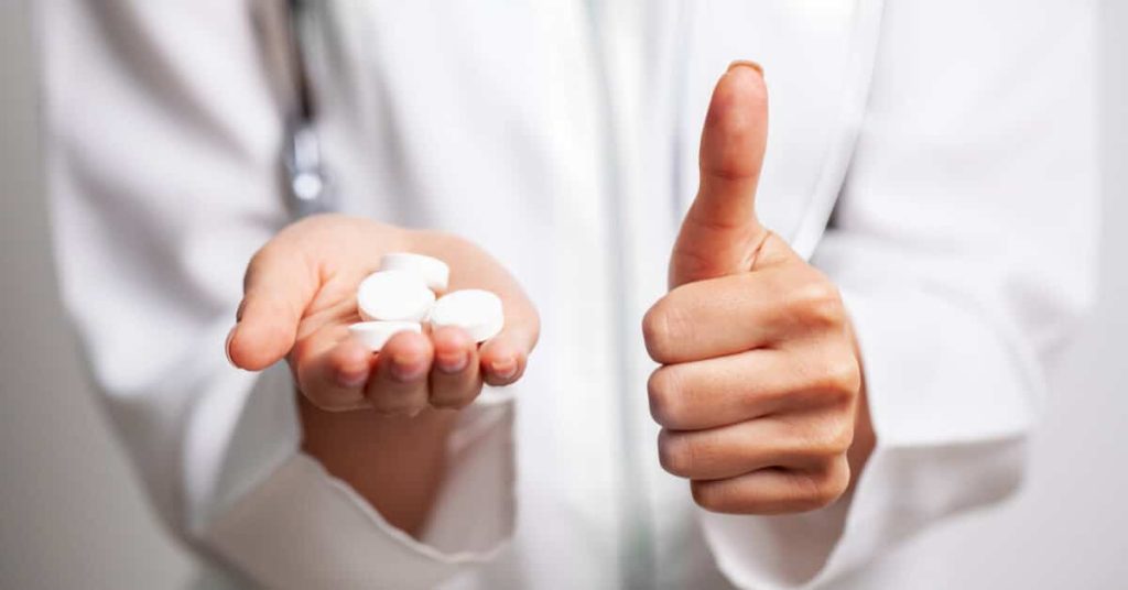 Clinician giving a thumbs-up with medication in one hand.