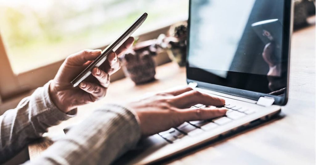 close up of hands working on a laptop and holding mobile device