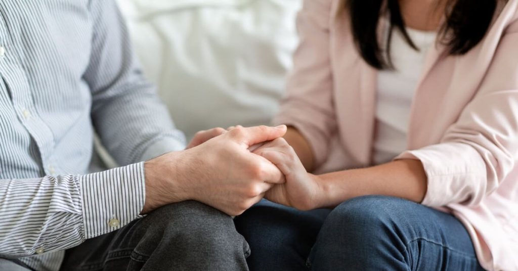 Closeup of a man and woman seated and holding hands