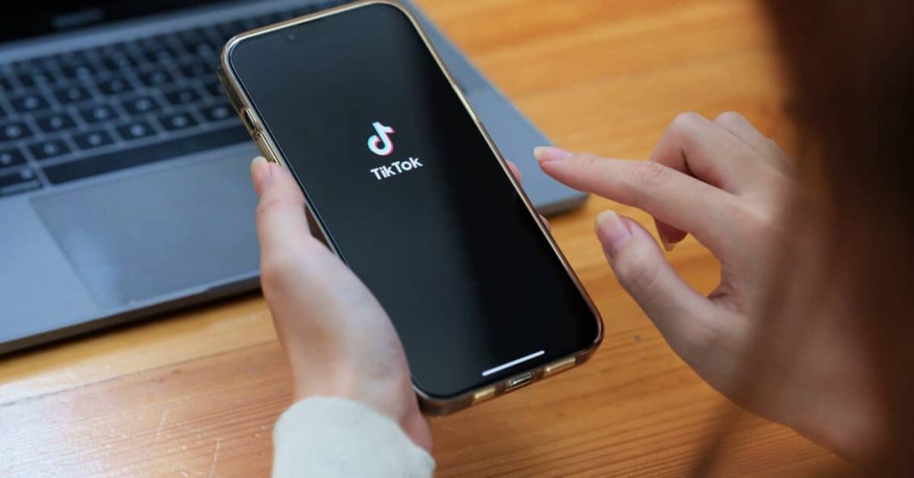 Hands opening the TikTok app on a mobile phone.