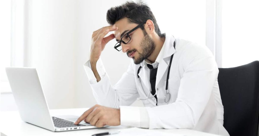 Frustrated doctor looking at a laptop screen.