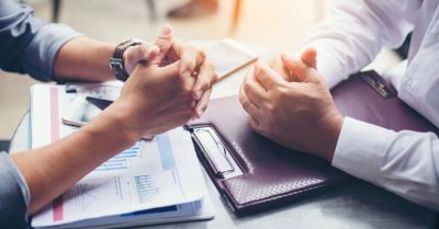 The arms of two business people leaning on a desk as they negotiate.