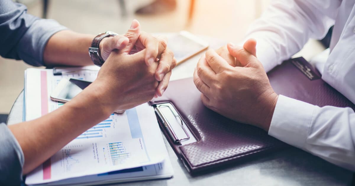 The arms of two business people leaning on a desk as they negotiate.