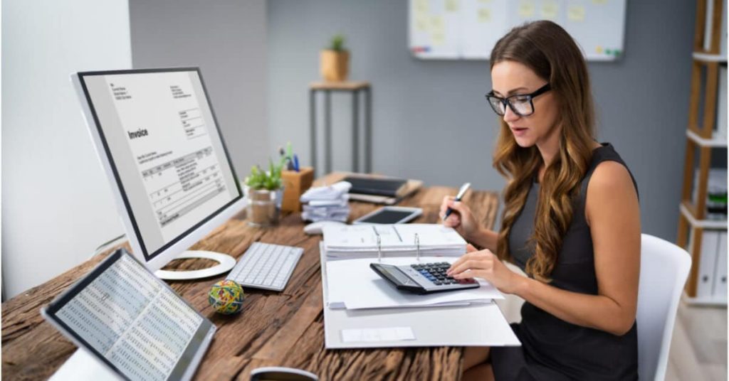 A woman sitting at a desk reviewing healthcare invoices.