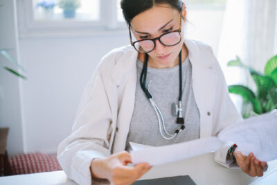 Female nurse practitioner in white coat reviewing a collaborating physician agreement at her desk.