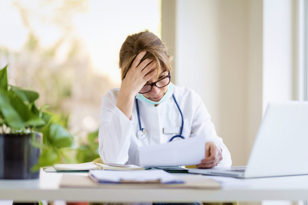Female physician in a white coat reviewing Medicare audit paperwork at her desk.