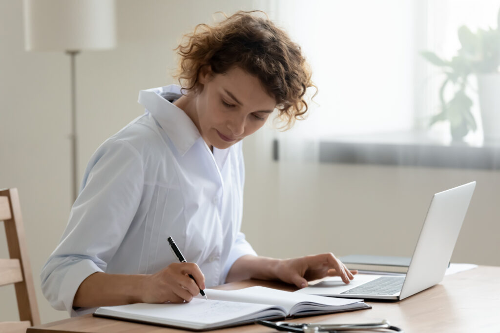 Healthcare provider in a white coat taking notes at her desk while planning Illinois PLLC formation for her practice.