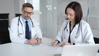 Two physicians in white coats reviewing and signing partnership documents.