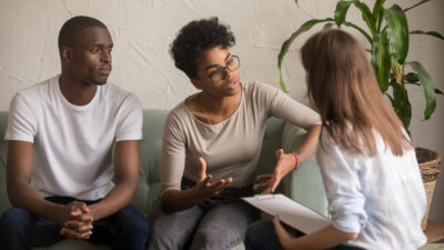 Couple on a couch meeting with a therapist about confidentiality in couples therapy.