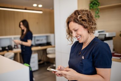 Smiling healthcare employee in navy scrubs checks social media on her phone, raising freedom of speech questions for private practices.