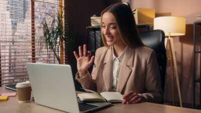 Therapist waving to a client during a telehealth video session on a laptop, a scenario Illinois providers face when a client moves out of state
