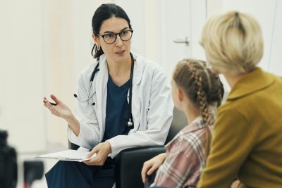 Pediatrician in white coat consulting with a young patient and parent during an office visit