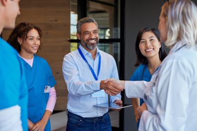 A woman physician shakes hands with an MSO representative as healthcare professionals discuss concierge medicine and DPC practice structures