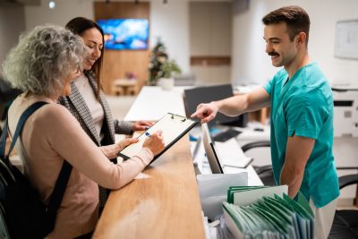 A physician discusses a direct primary care agreement with patients at a medical clinic reception desk.